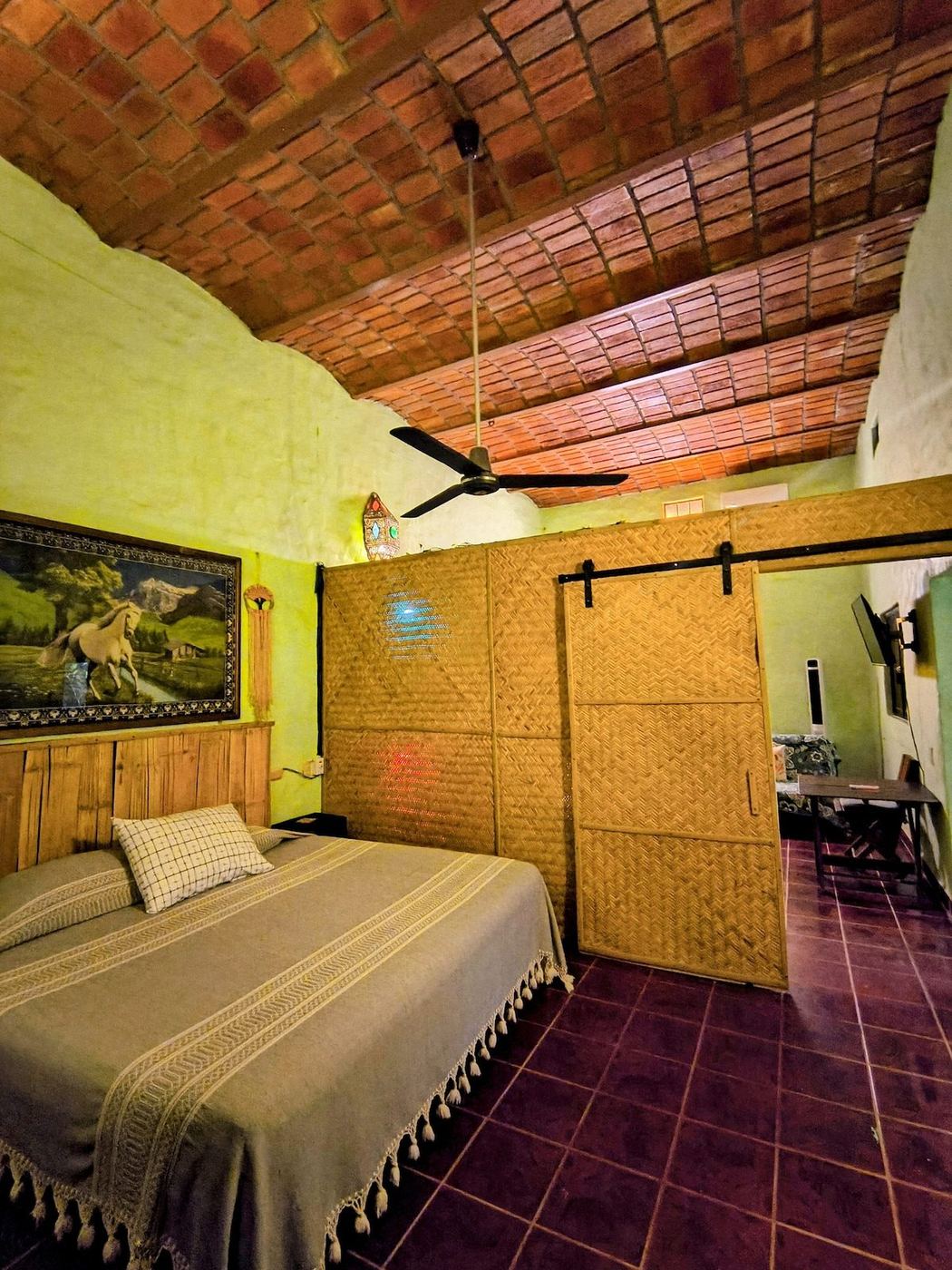 A bedroom at La Casa Grande, brick ceiling, clay tile floor, and a woven sliding door