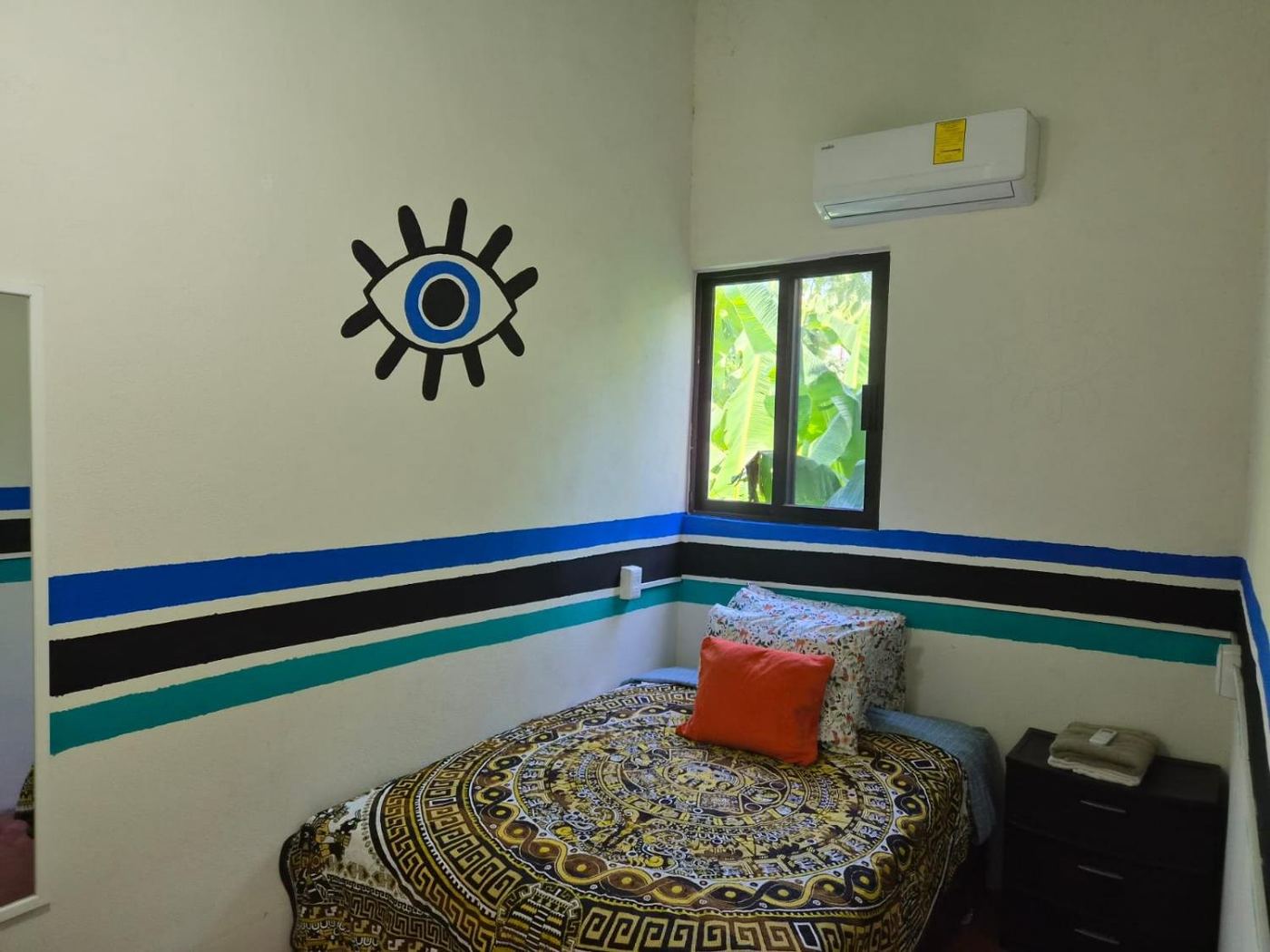 The bedroom at Two bedroom Delight, a painted eye above the bed and banana leaves in the window