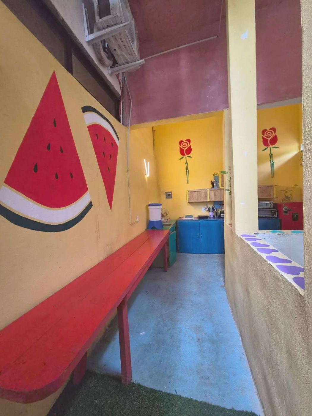 The terrace at Two bedroom Delight, watermelon slices on a yellow wall and a red bench