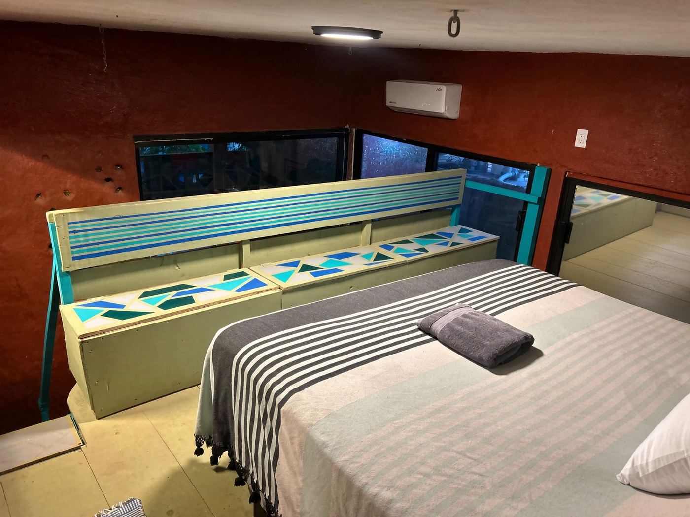 The upstairs bed at El Loft, a striped blanket and a painted geometric railing