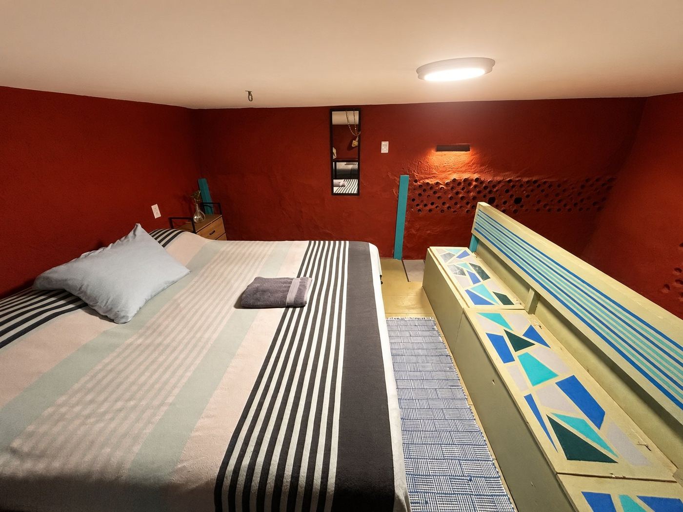 The loft bedroom, red walls, a striped bed, and the painted bench beside it