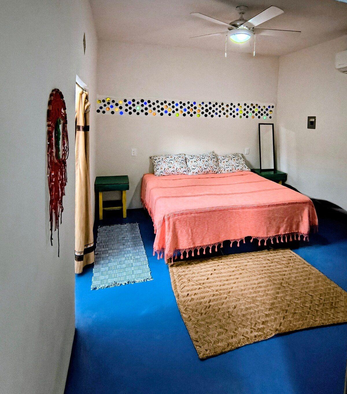 The bedroom at Casita Sol, a coral spread on a blue floor