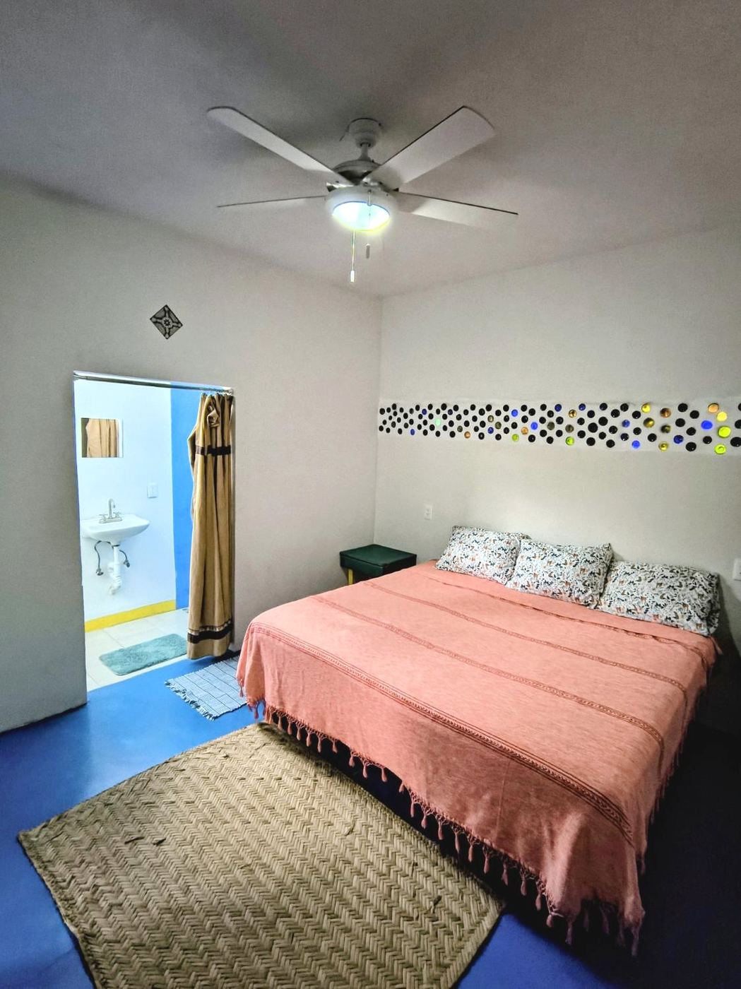 The bedroom at Casita Sol, a coral spread, a woven rug, and a blue floor