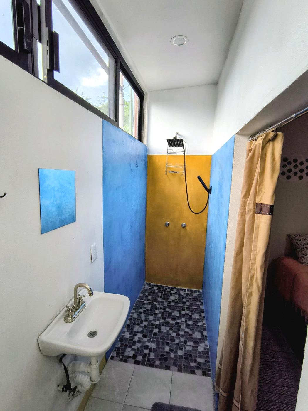 The shower at Casita Sol, blue walls, a gold accent, and a mosaic floor